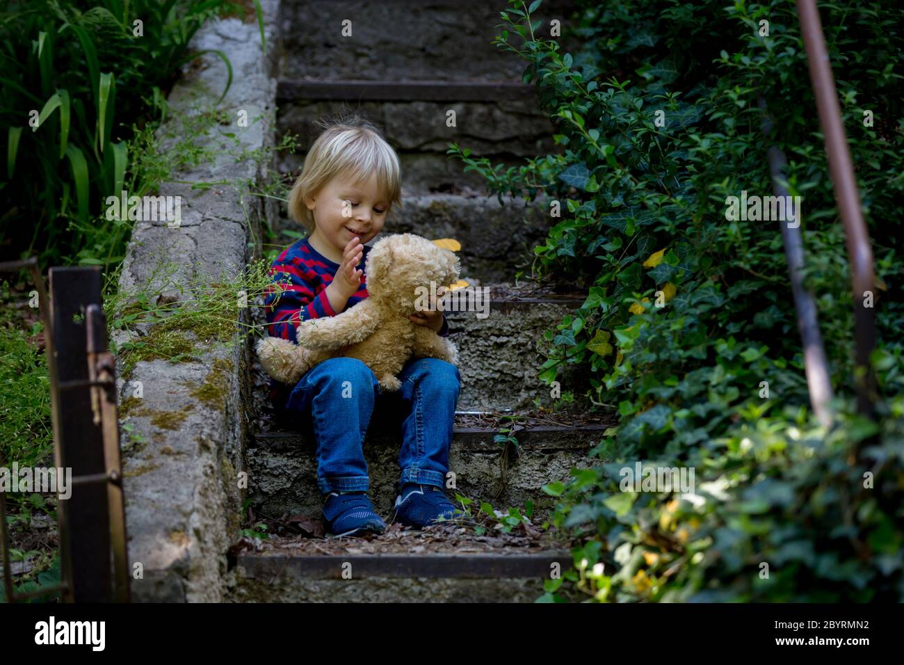 Cute little todller boy, sitting on stairs with teddy bear, playing ...