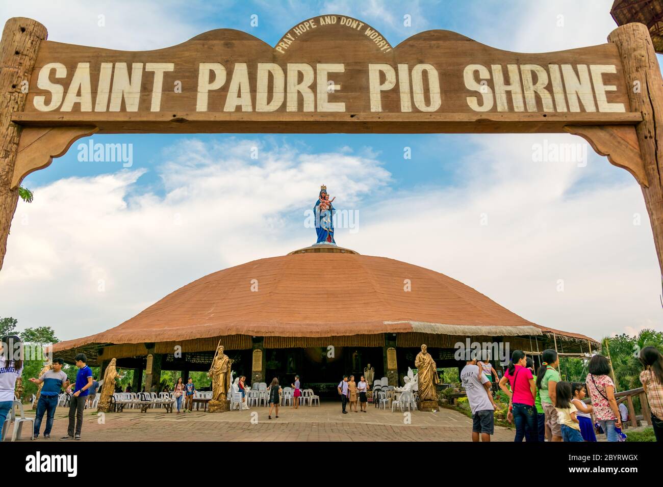 Sto. Tomas Batanga/ Philippines- 31 May 2015: Virgin Mary stats on top of the roof of Padre Pio shrine. Church goers gather in front of the church. Stock Photo