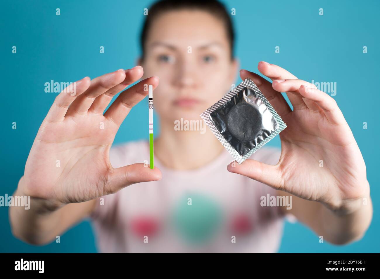 A young girl holds out a condom and a positive pregnancy test Stock Photo
