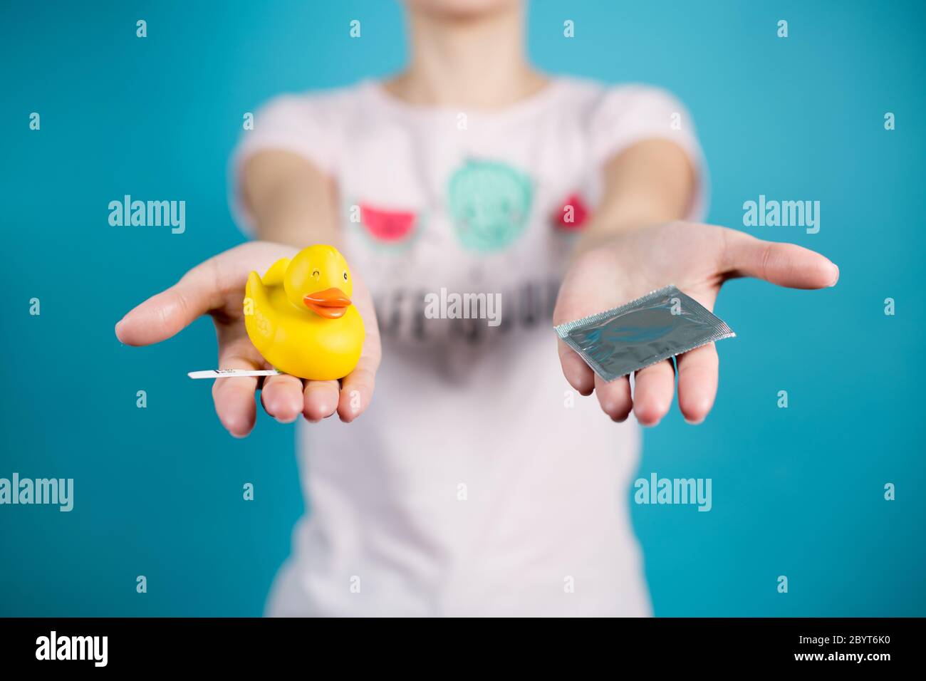 A young girl holds out a condom and a toy duck with a pregnancy test Stock Photo