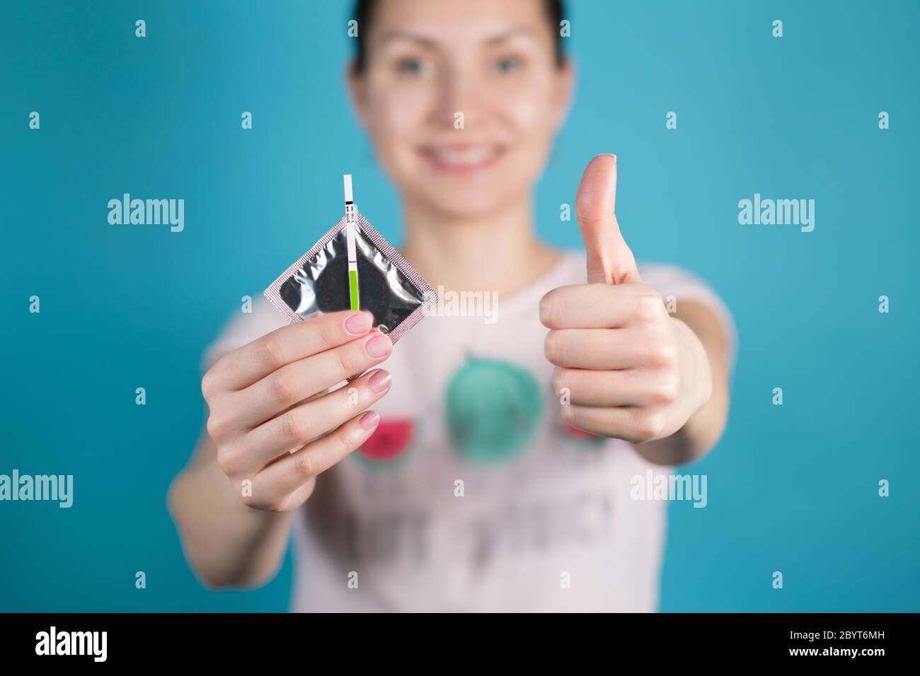 A young girl holds out a condom and a negative pregnancy test into the camera Stock Photo