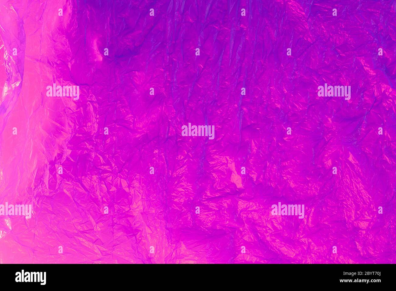 Background from purple recyclable polyethylene in neon pink light. Eco, zero waste, alternative to plastic concept. Flat lay. Horizontal. Closeup. Stock Photo