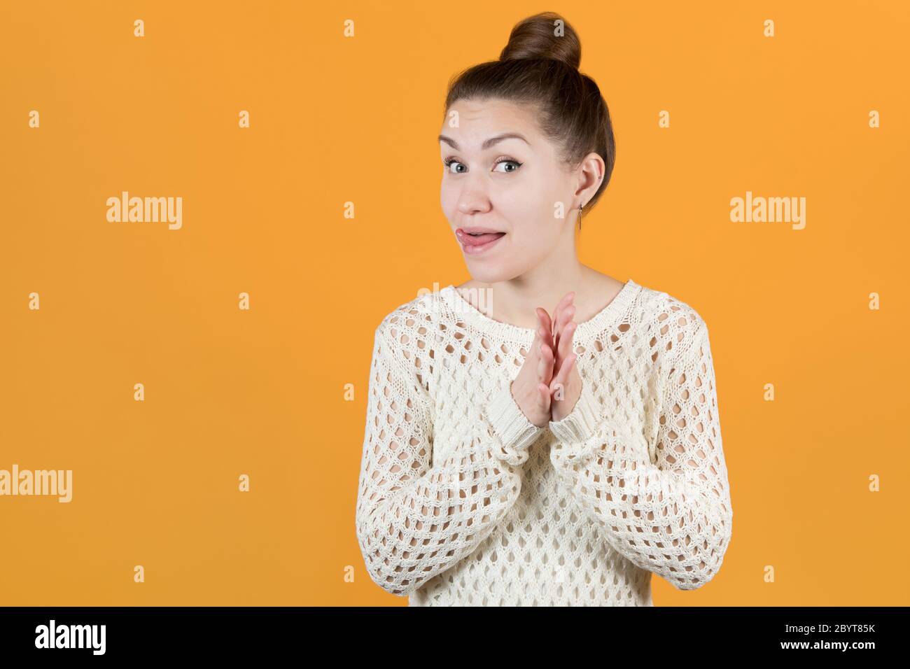 girl looks slyly at the camera, rubbing her hands and sticking out her tongue Stock Photo