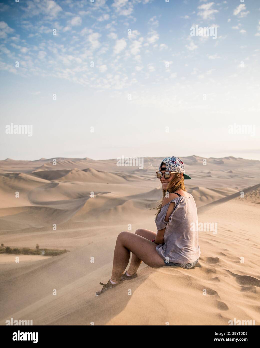 woman sitting on a top of a dune, smiling and clouds Stock Photo