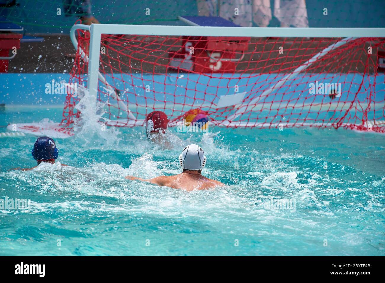 A water polo player scores a goal, goalkeeper misses the ball went into the net Stock Photo