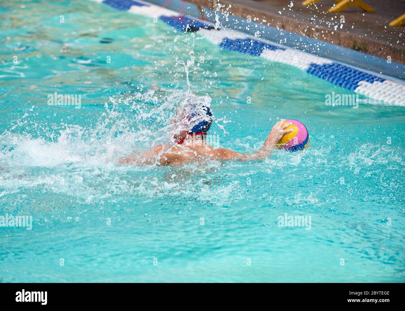Water polo player in a swimming pool getting splashed with water ready to throw a ball Stock Photo