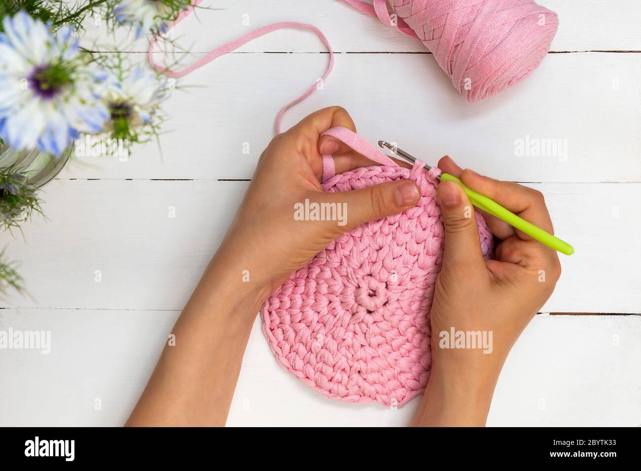 Directly above view of woman hands holding crochet hook and crocheting with ribbon yarn on white wooden table Stock Photo