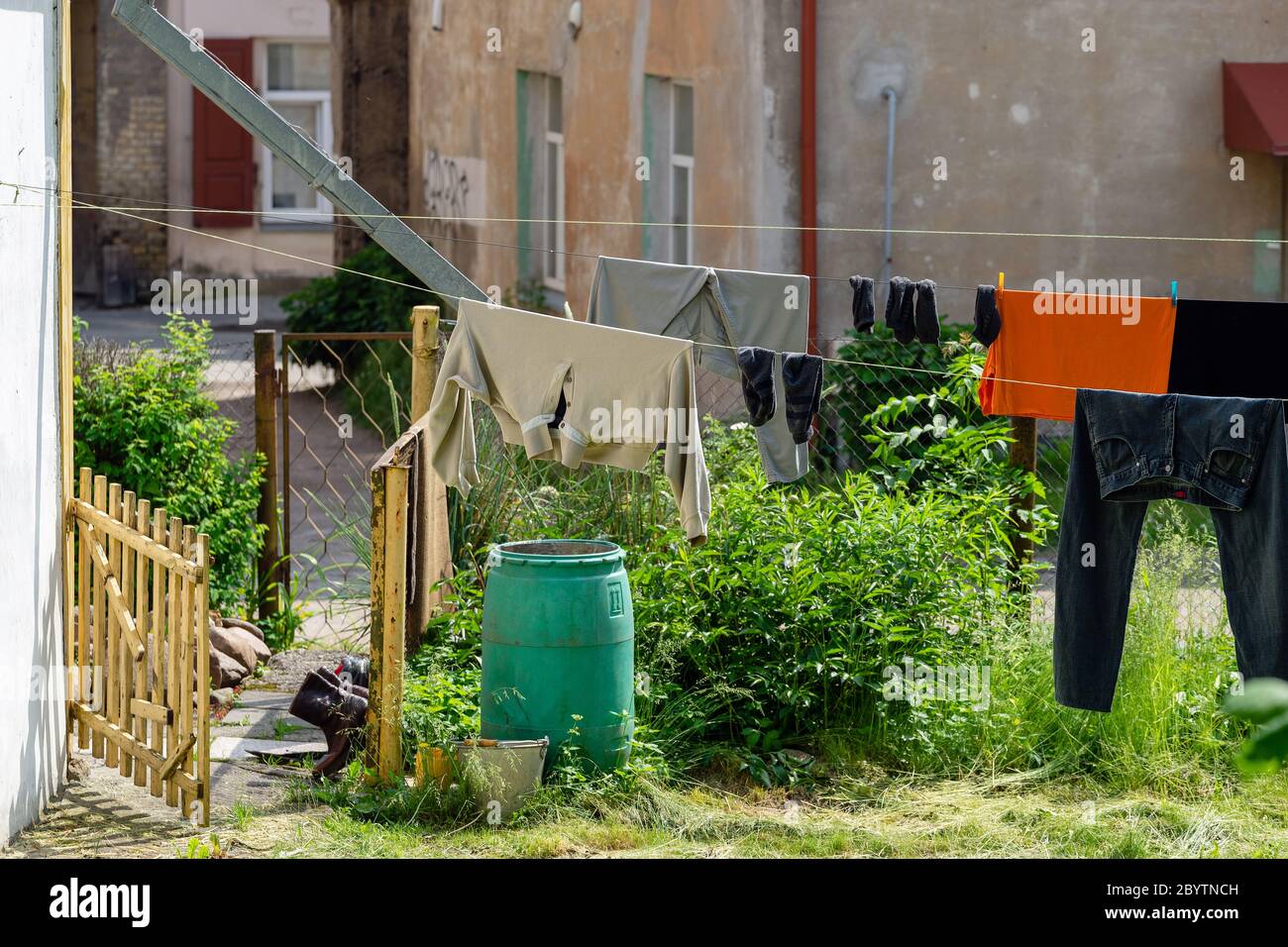 Clean different laundry are dried outside in the yard on a clothing line in the city. Black shoes are ventilated at the gates. On blurred old houses b Stock Photo