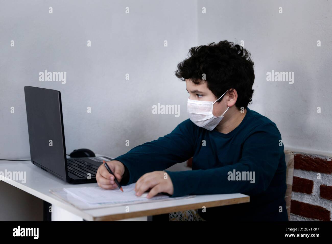 white young boy improvises study with computer and wearing respiratory protection mask Stock Photo