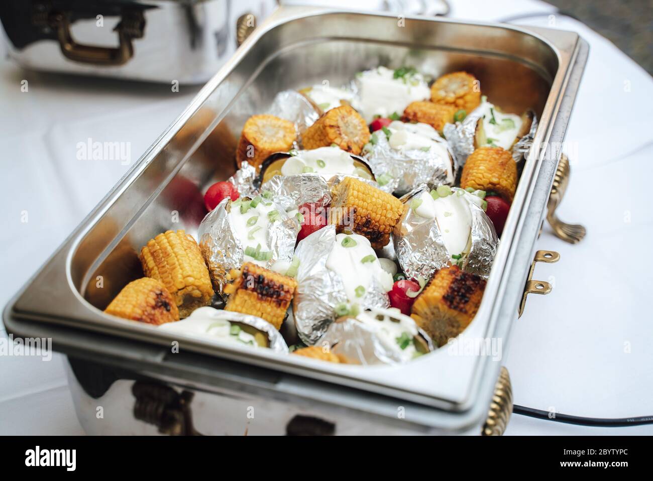 https://c8.alamy.com/comp/2BYTYPC/grilled-corn-and-baked-potatoes-stuffed-with-cheese-in-hotel-pan-on-food-warmer-self-service-buffet-table-celebration-party-birthday-or-wedding-2BYTYPC.jpg