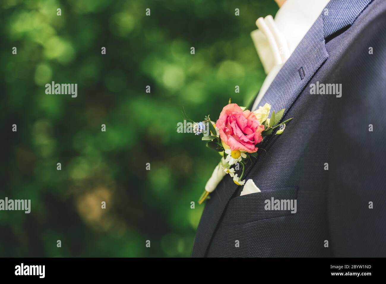 Colorful wedding boutonniere on lapel of groom's blue jacket. Side view of small posy decoration. Blurred lush green foliage background. wedding day Stock Photo