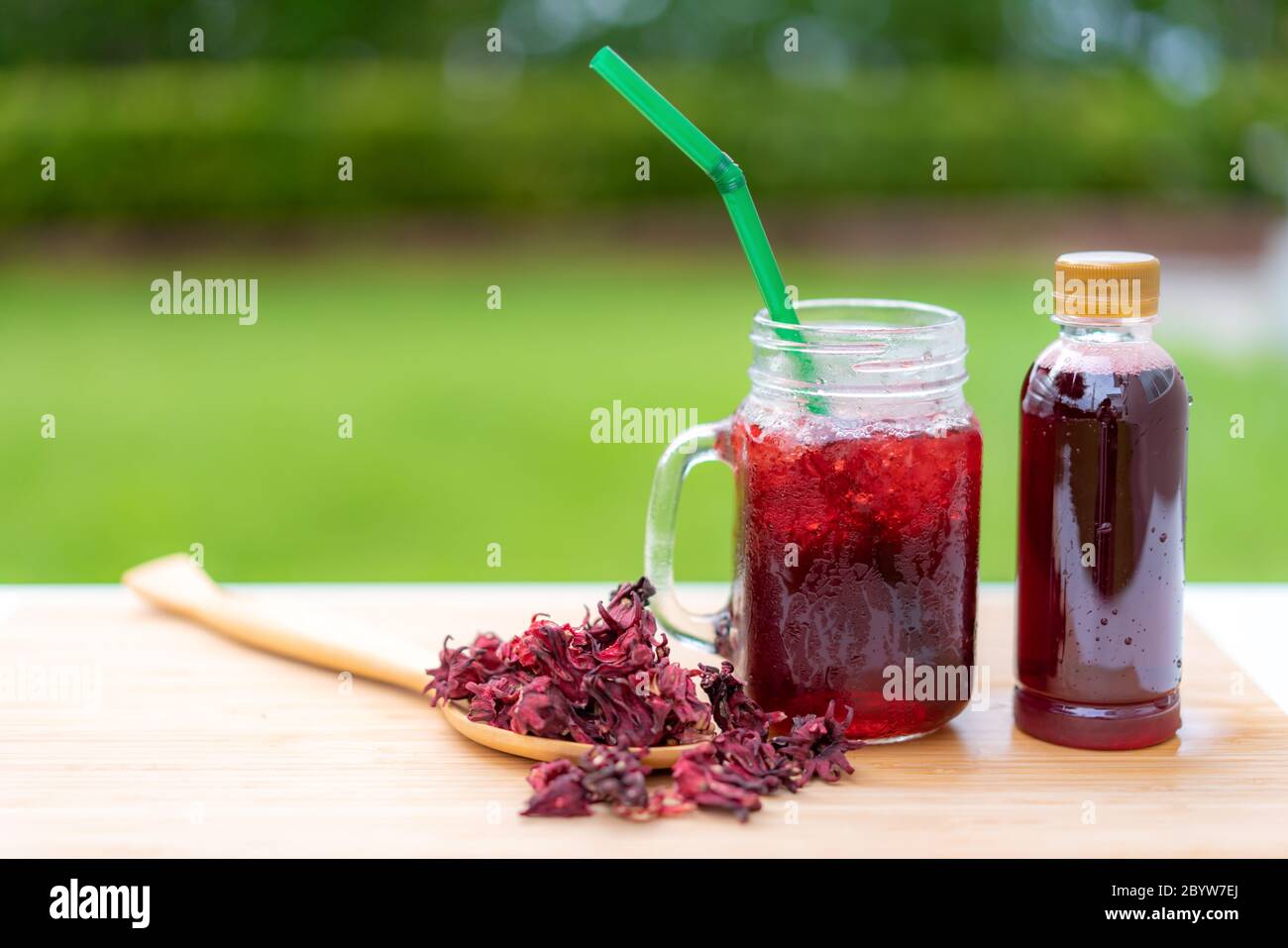 Cold beverage glass of roselle juice with colorful straw in wooden table Thai herb juice and refreshment cold drink. Stock Photo