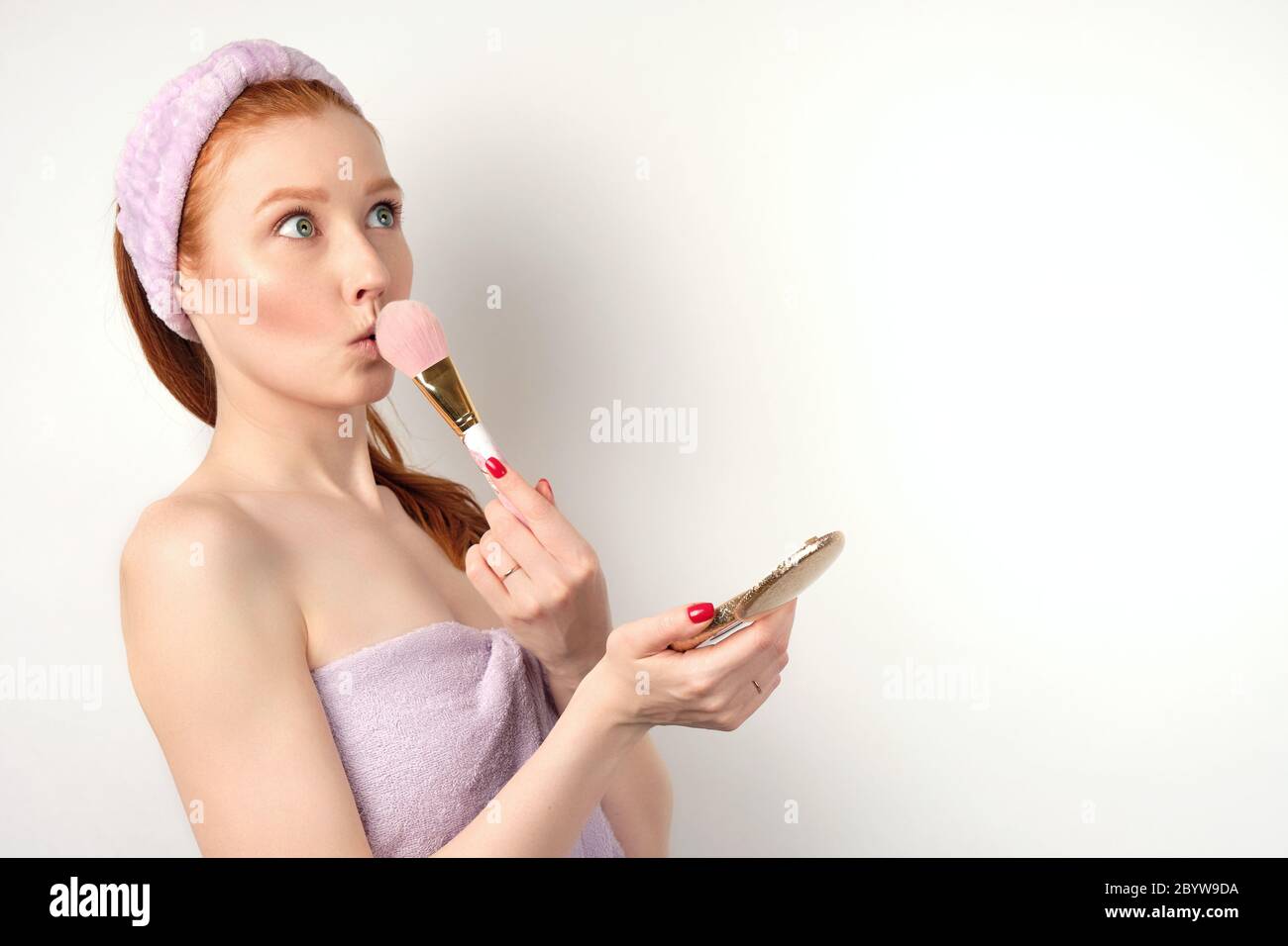 A red-haired girl is standing on a white background in a towel, Stock Photo