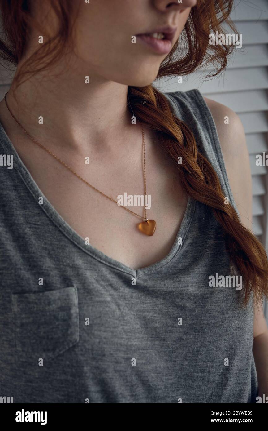 Close frame of a heart-shaped pendant on the chest of a red-haired girl with a scythe, focus on the pendant Stock Photo