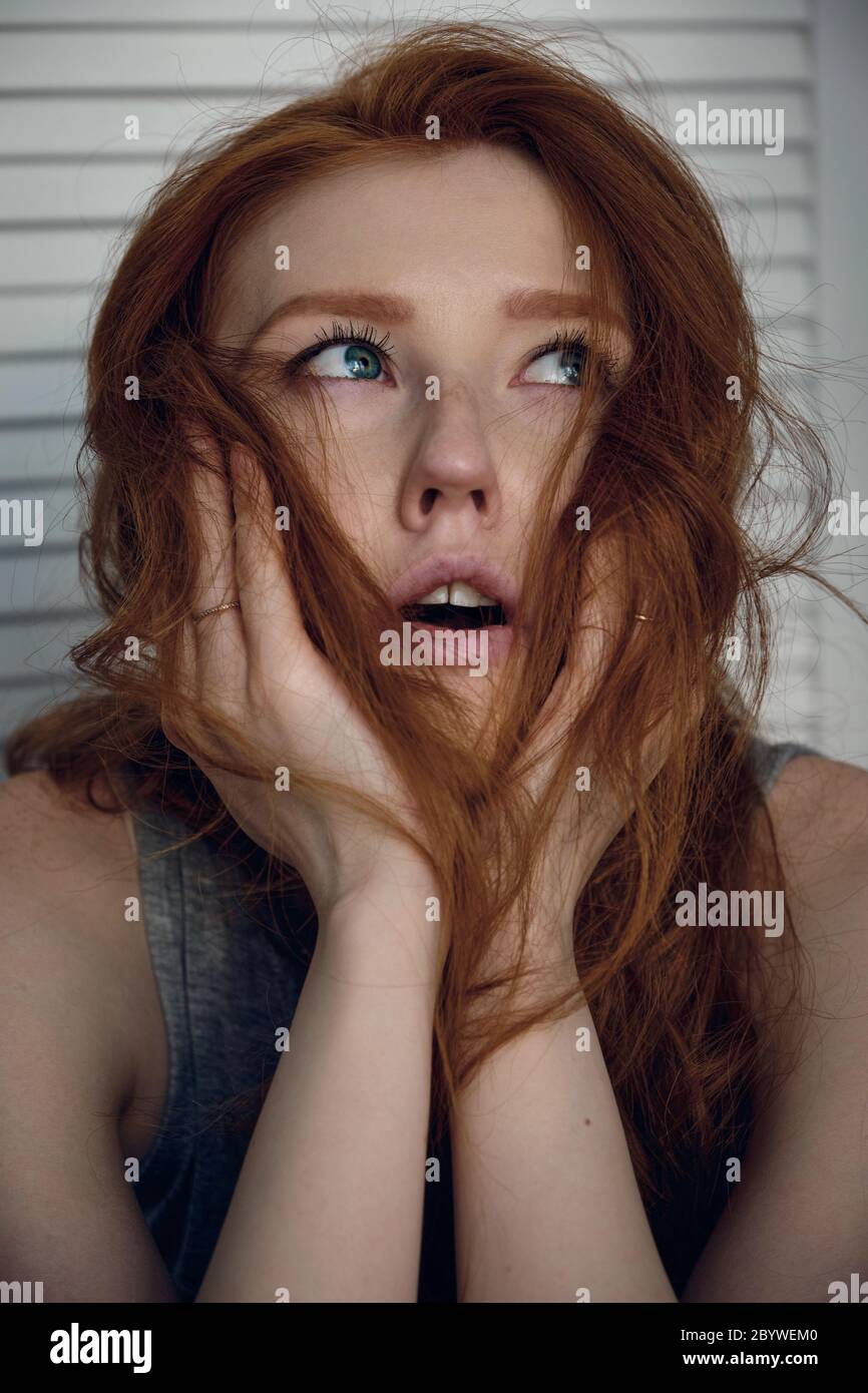 Headshot. The red-haired girl looks up, opening her mouth and pressing her hands to her face. Stock Photo