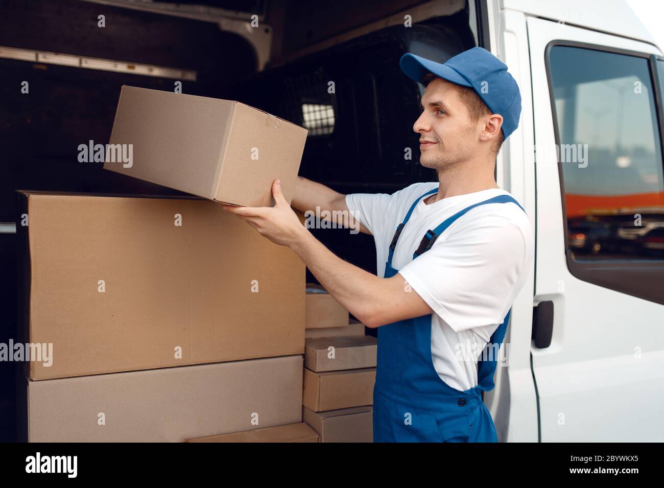 Smiling deliveryman with carton box at the car, delivery service. Man