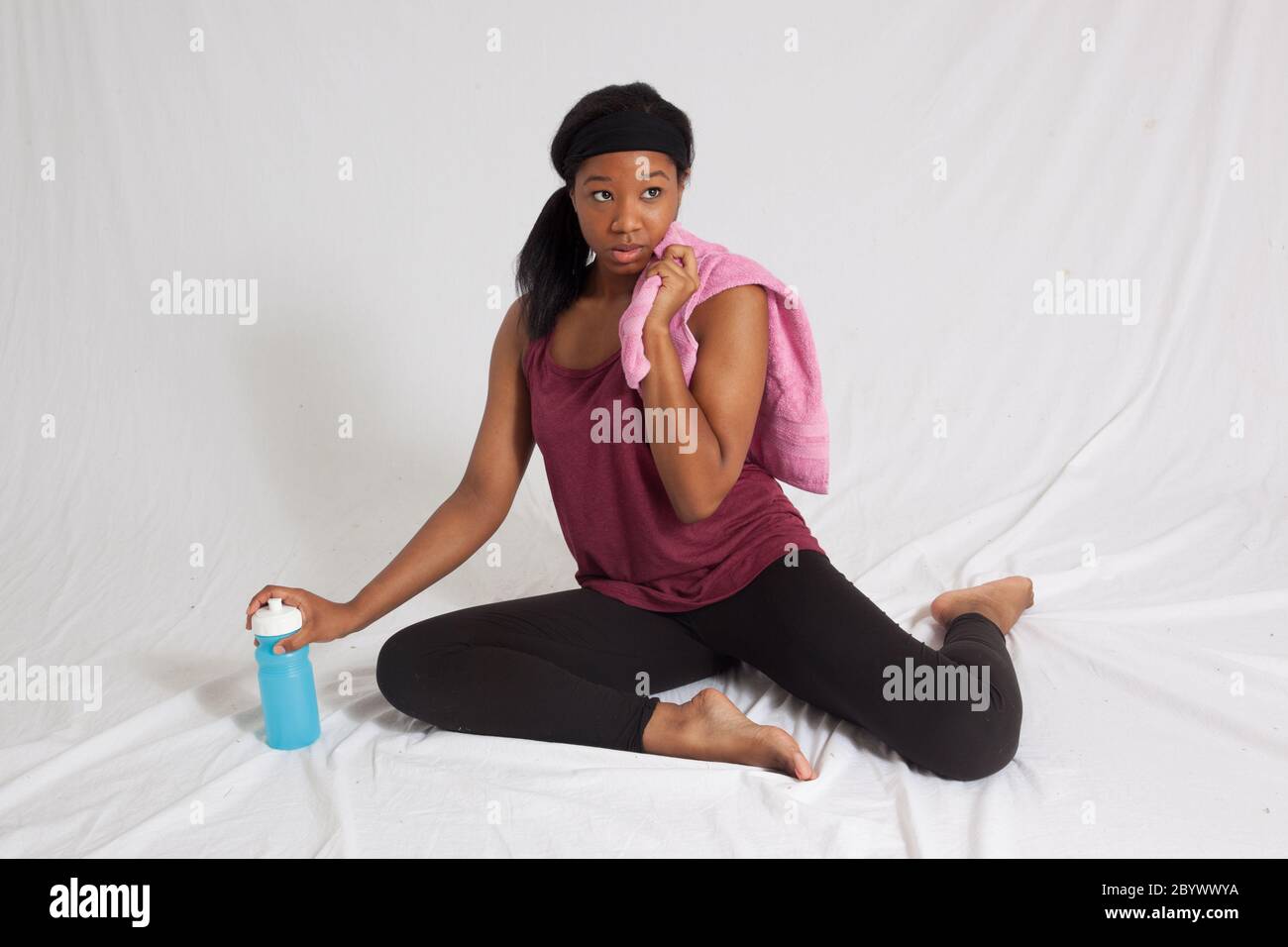 Happy Black woman sitting in an exercise outfit, towel and water bottle ...