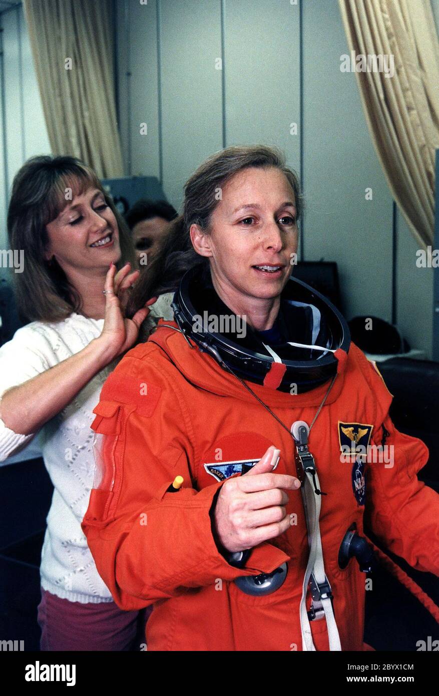 STS-81 Mission Specialist Marsha S. Ivins gets a helping hand from a suit technician as she prepares to don the helmet of her launch/entry suit in the suitup room of the Operations and Checkout (O&C) Building. She is the veteran of three Shuttle flights and became an astronaut in 1984. Among other responsibilities, Ivins will perform photo and video surveys of the Russian Mir space station and operate the Kidsat experiment camera on the orbiter’s aft flight deck. She and five crew members will shortly depart the O&C and head for Launch Pad 39B, where the Space Shuttle Atlantis will lift off du Stock Photo