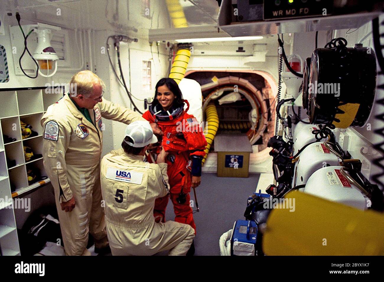 STS-87 Mission Specialist Kalpana Chawla, Ph.D., is assisted with her ascent and re-entry flight suit in the white room at Launch Pad 39B by Danny Wyatt, NASA quality assurance specialist. Kneeing before Dr. Chawla to assist her is George Schram, USA mechanical technician, as Dr. Chawla prepares to enter the Space Shuttle orbiter Columbia on launch day. STS-87 is the fourth flight of the United States Microgravity Payload and Spartan-201 Stock Photo