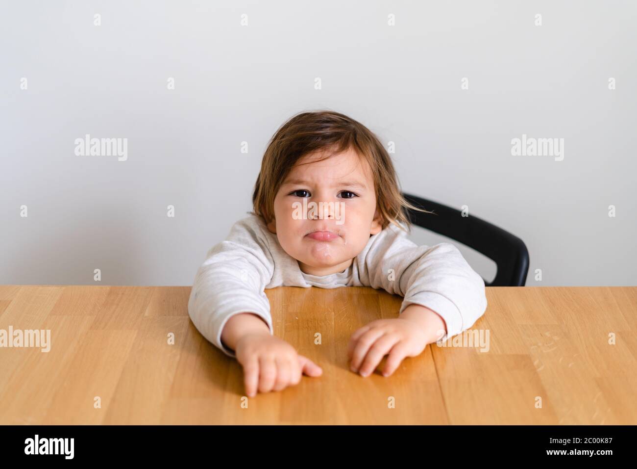 Toddler girl unhappy sitting at wooden desk. Tired child, hungry kid Stock Photo