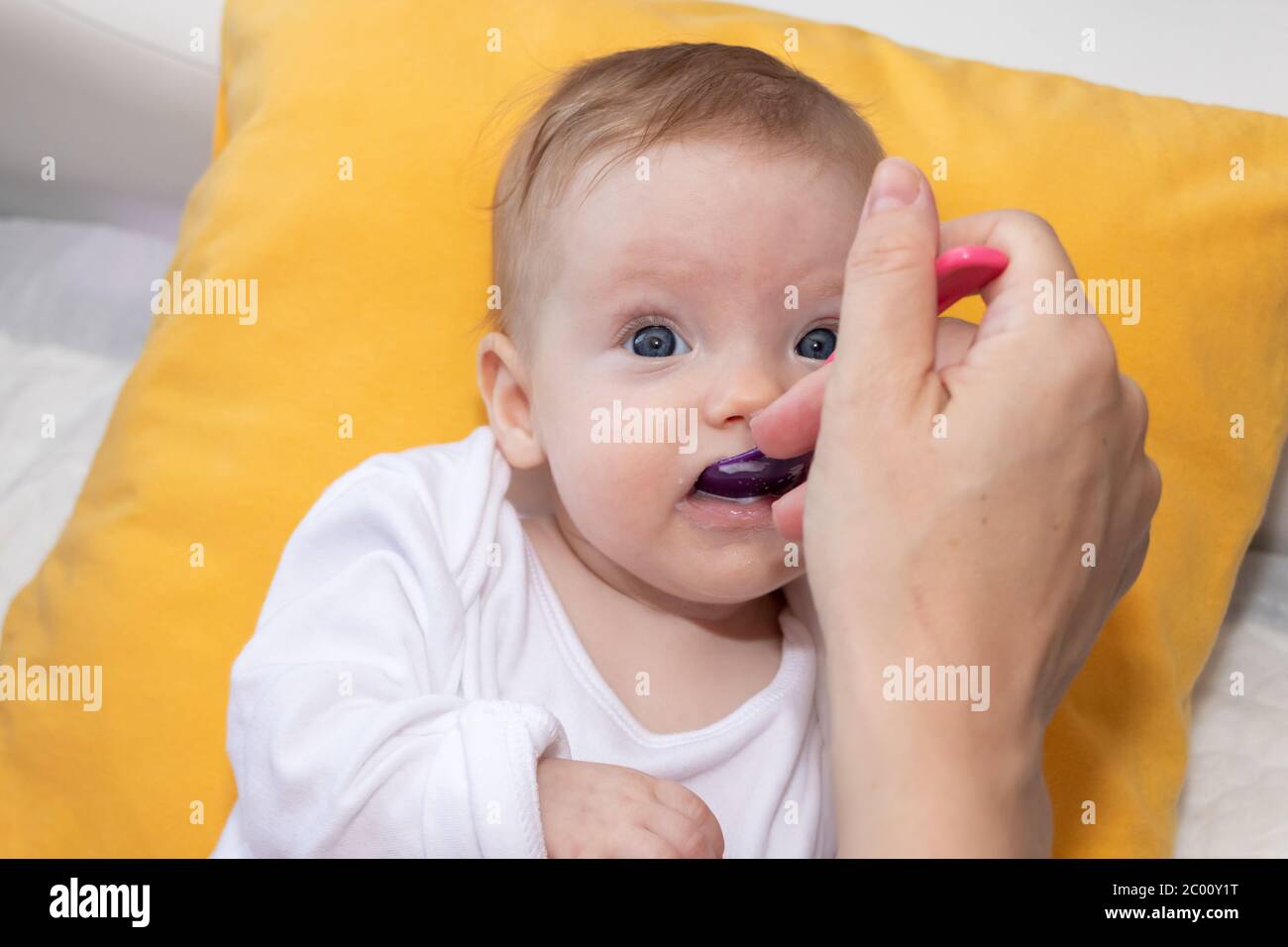 Cute little baby girl lying on the bed and eating rice soup with spoon
