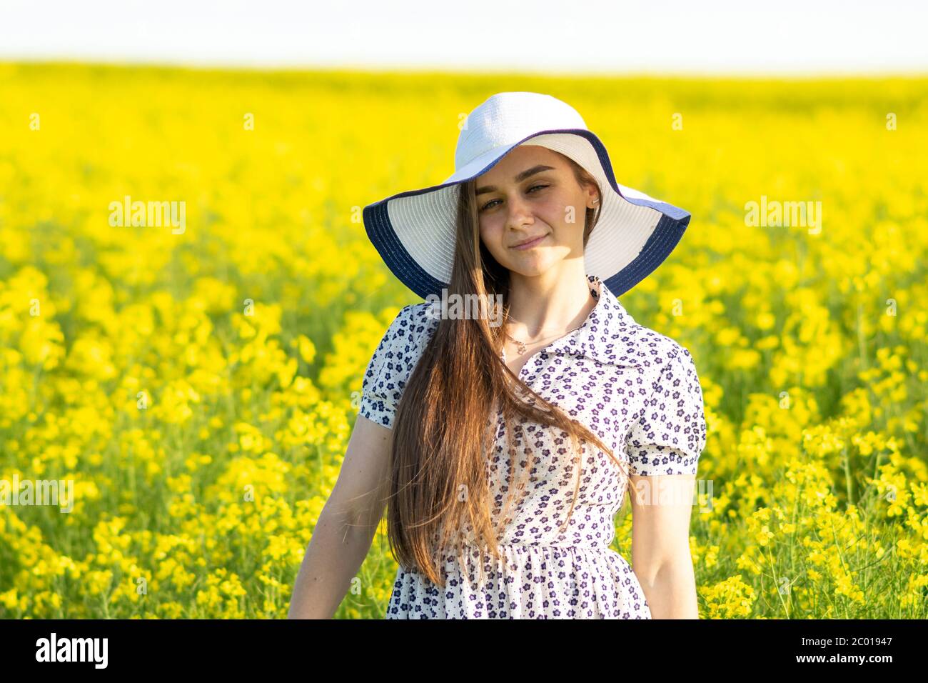 Beautiful girl in a rapeseed field, in a dress and hat Stock Photo - Alamy