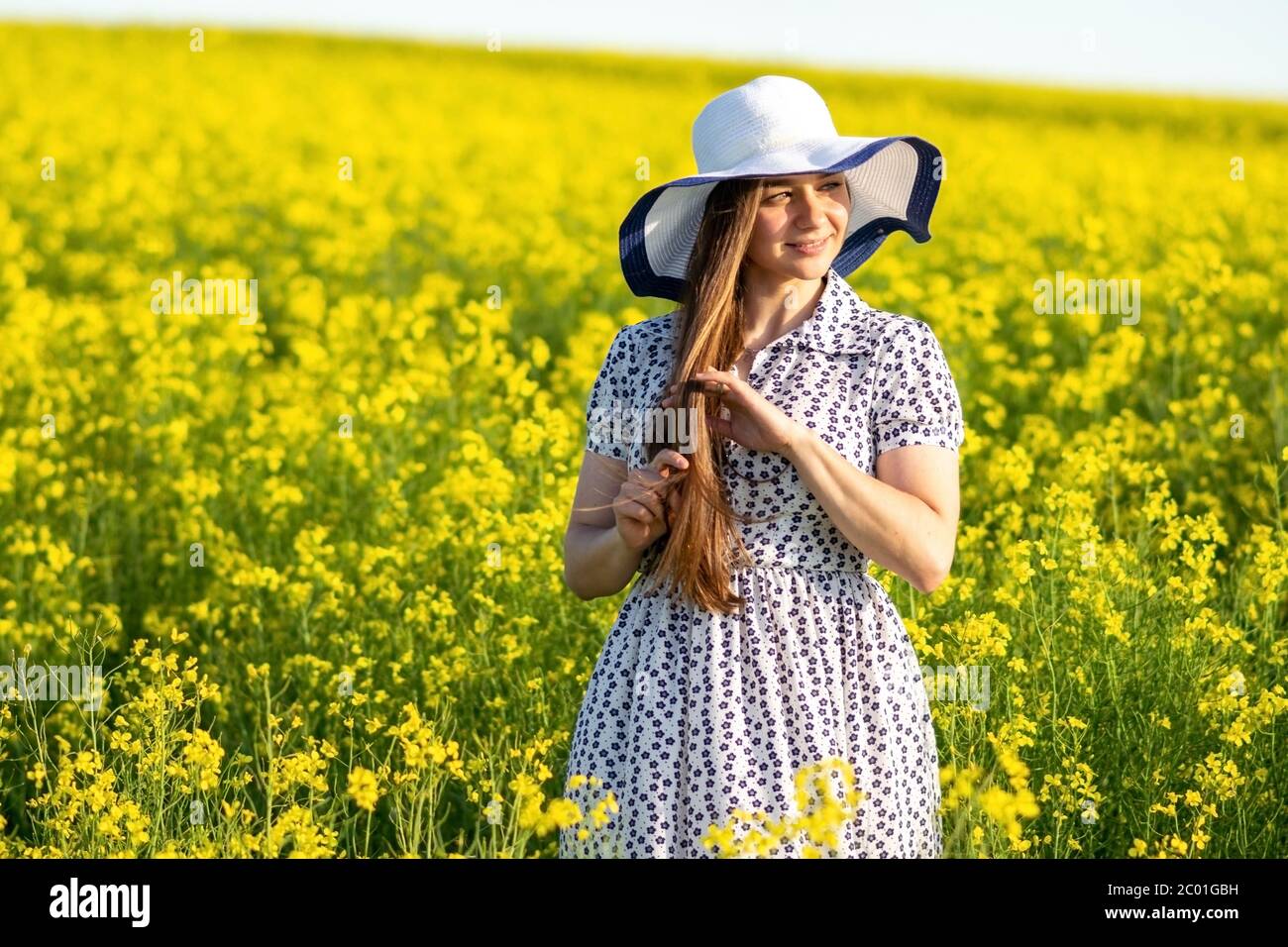 Beautiful girl in a rapeseed field, in a dress and hat Stock Photo - Alamy