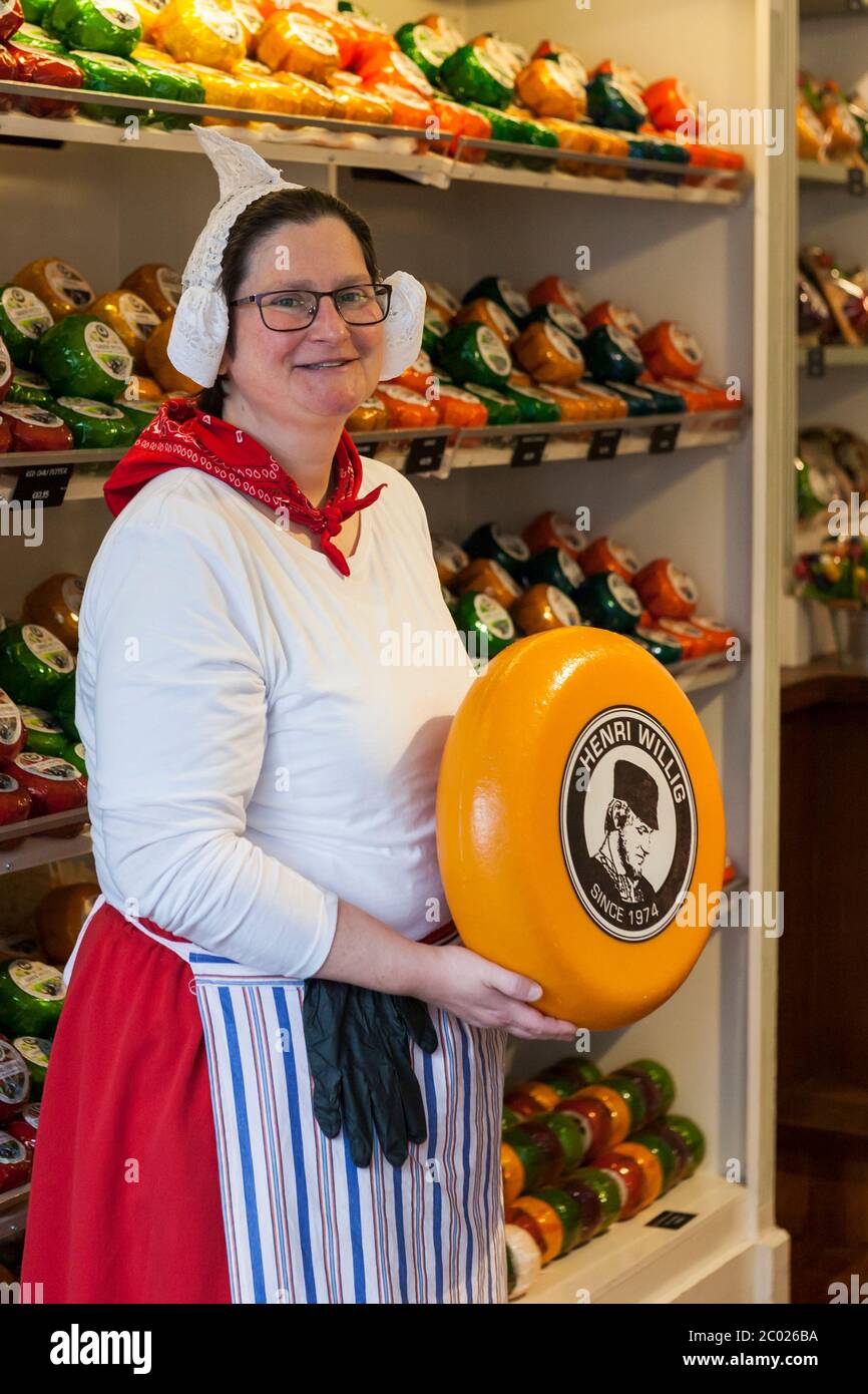 A salesperson in tradtional Dutch dress poses with a round of cheese, Henri Willig Cheeseshop, Markt, Delft, South Holland, Netherlands Stock Photo