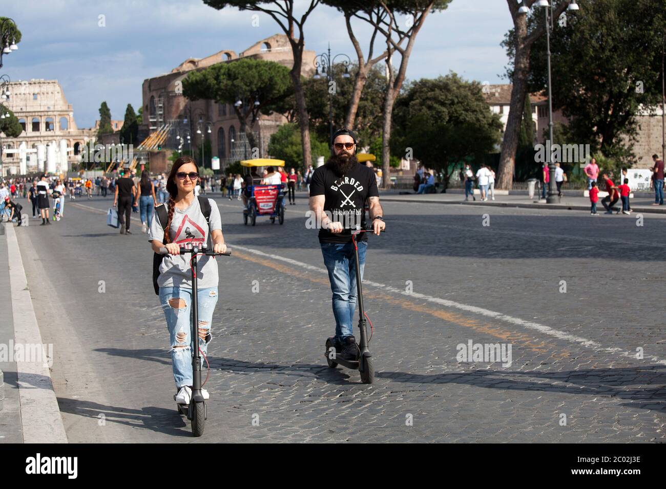 A couple of guys use electric scooters to commute in Via dei Fori Imperiali near Piazza Venezia in central Rome on June 02, 2020 as Italy starts to ease its lockdown, during the country's lockdown aimed at curbing the spread of the COVID-19 infection, caused by the novel coronavirus. Stock Photo