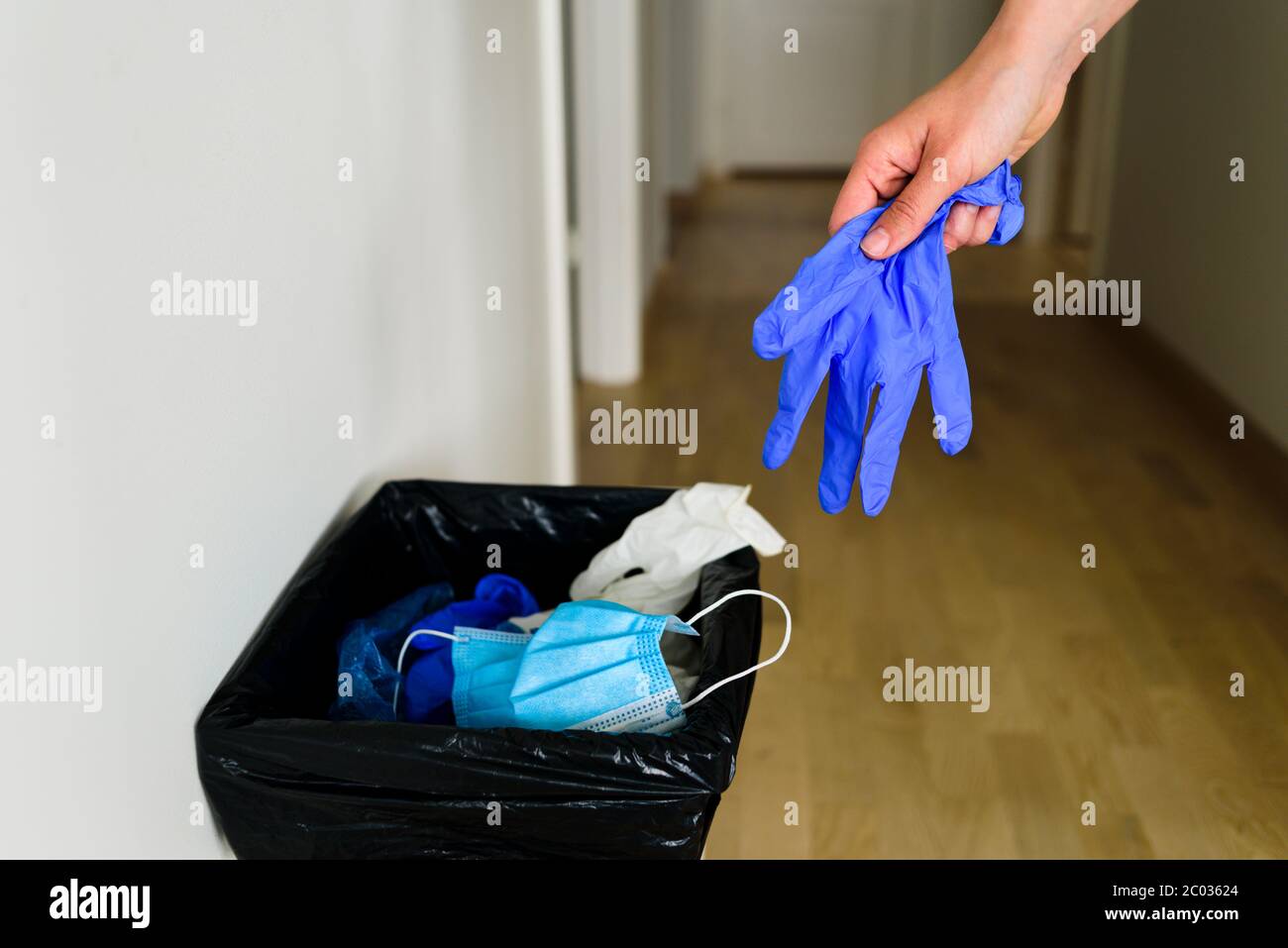 Hand throwing glove to container with medical garbage face mask