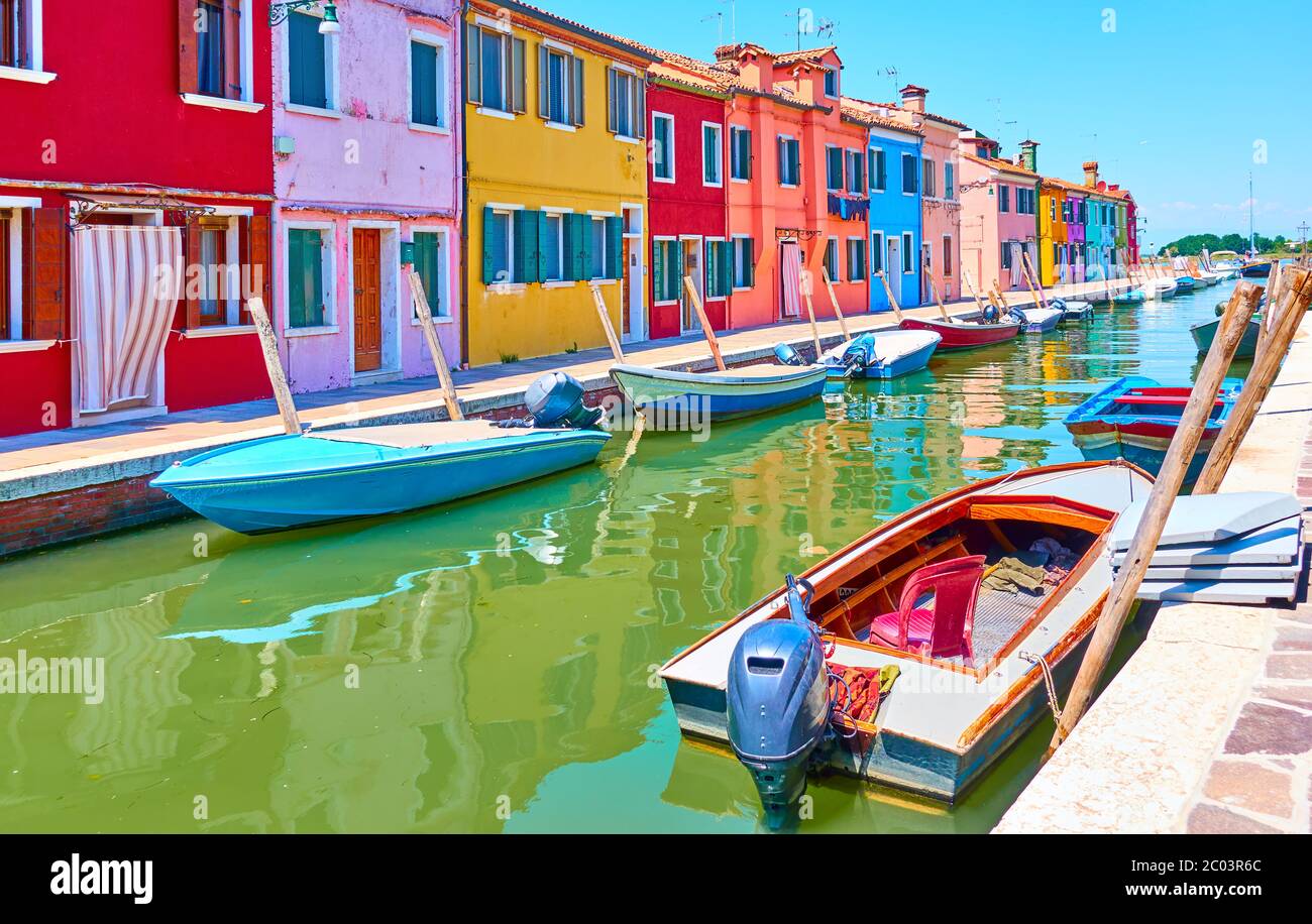 Perspective of canal with moored motorboats and colorful houses in Burano in Venice, Italy - Italian view Stock Photo