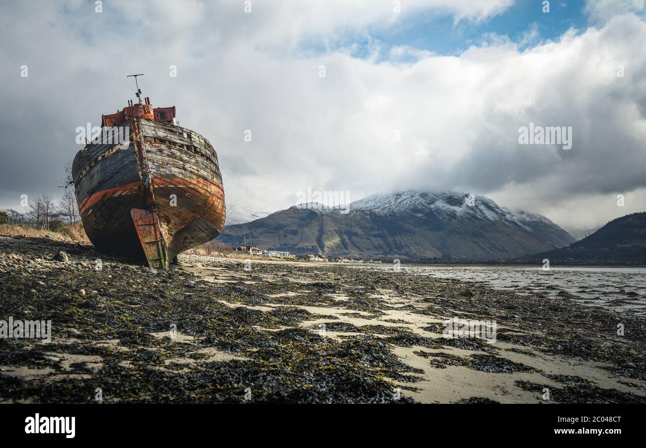 Ship wreck on the beach at low tide. The Old Boat of Corpach, Ben Navis on Loch Eil near Fort William in Scotland. Stock Photo