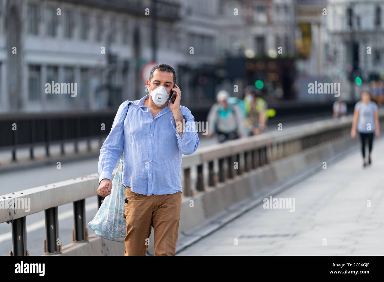 Middle aged Middle Eastern Arabic man walking along Waterloo Bridge in London, England wearing a face mask and talking on his mobile phone Stock Photo