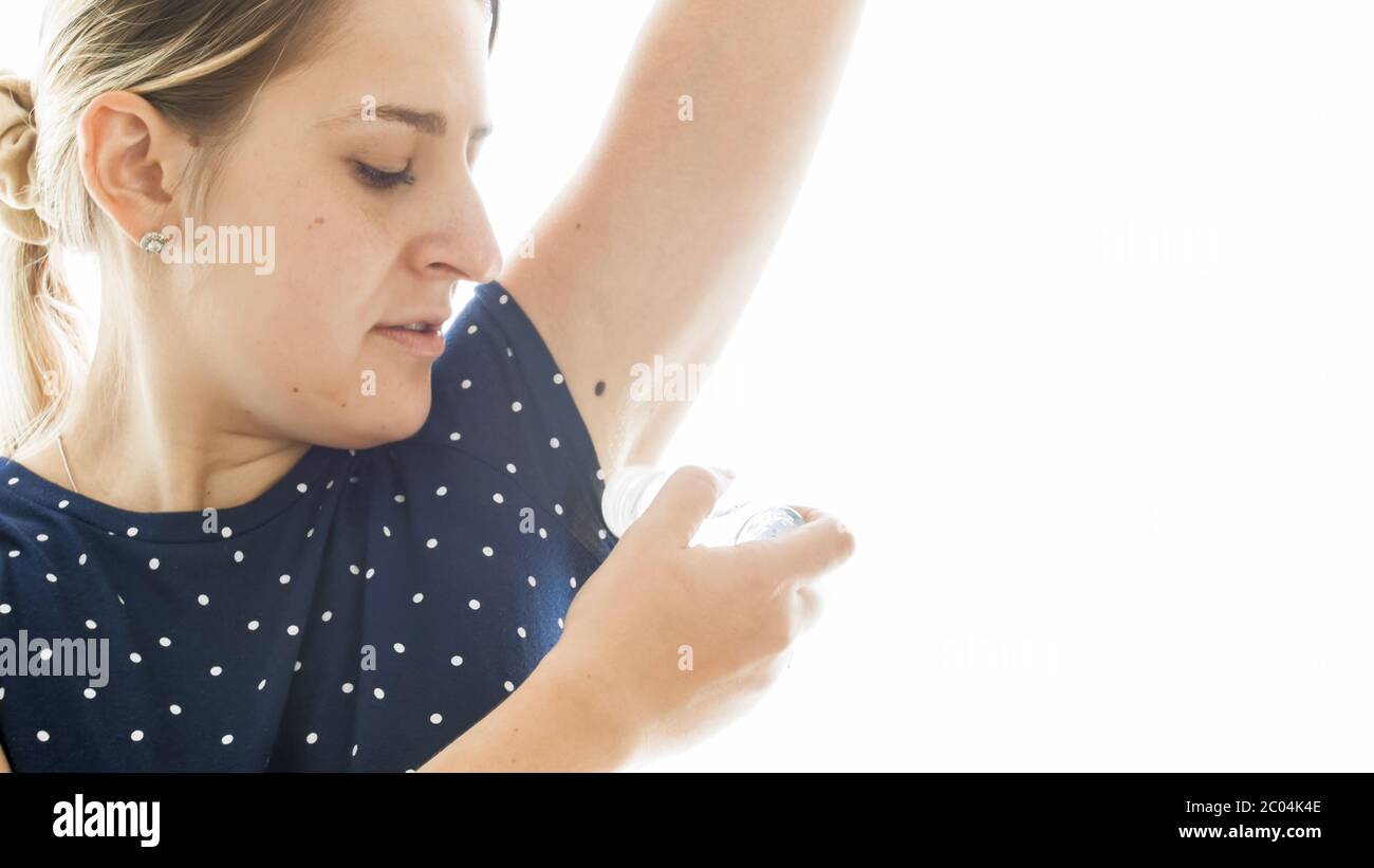 Portrait of young woman applying deodorant on sweaty armpits over white