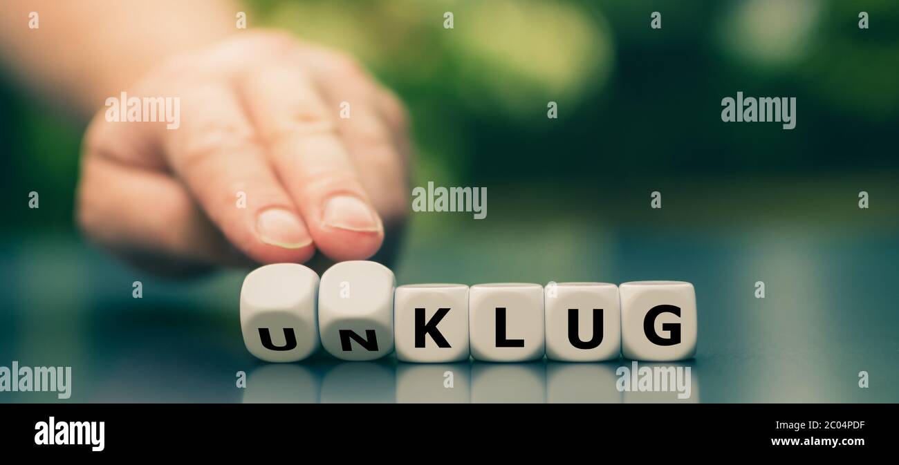 Hand turns dice and changes the German word 'unklug' ('stupid') to 'klug' ('smart'). Stock Photo
