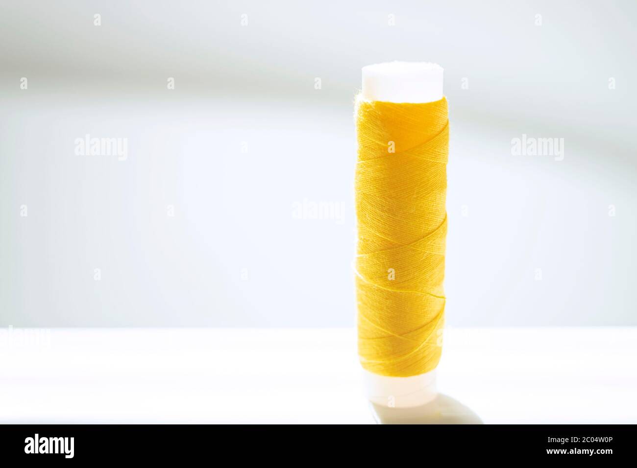 Yellow thread spool on a white bright table. Stock Photo