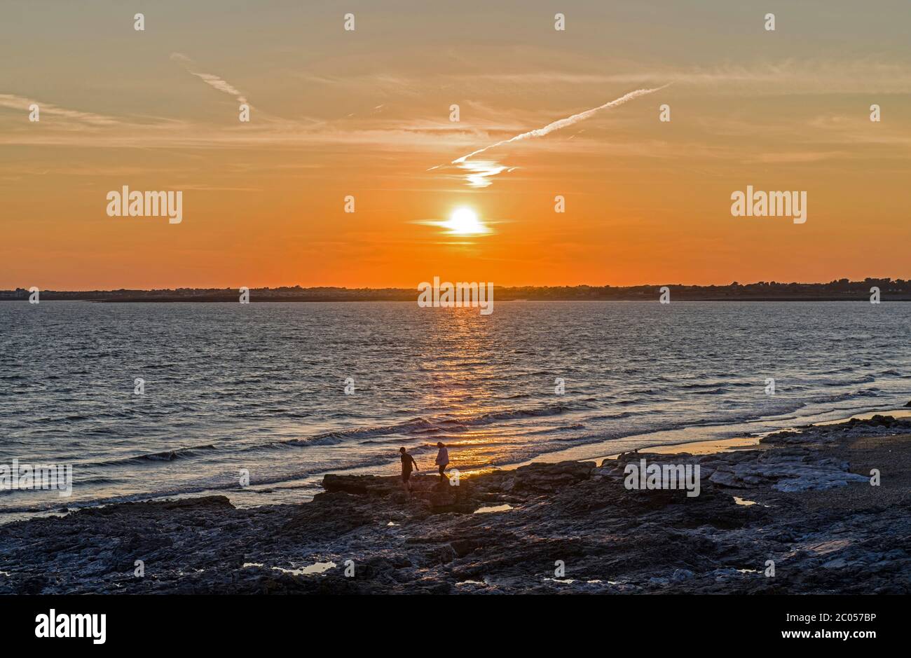 Setting sun over Porthcawl on the south Wales coast. Photograph taken from Ogmore by Sea beach on a summer evening. Two people on the seashore. Stock Photo