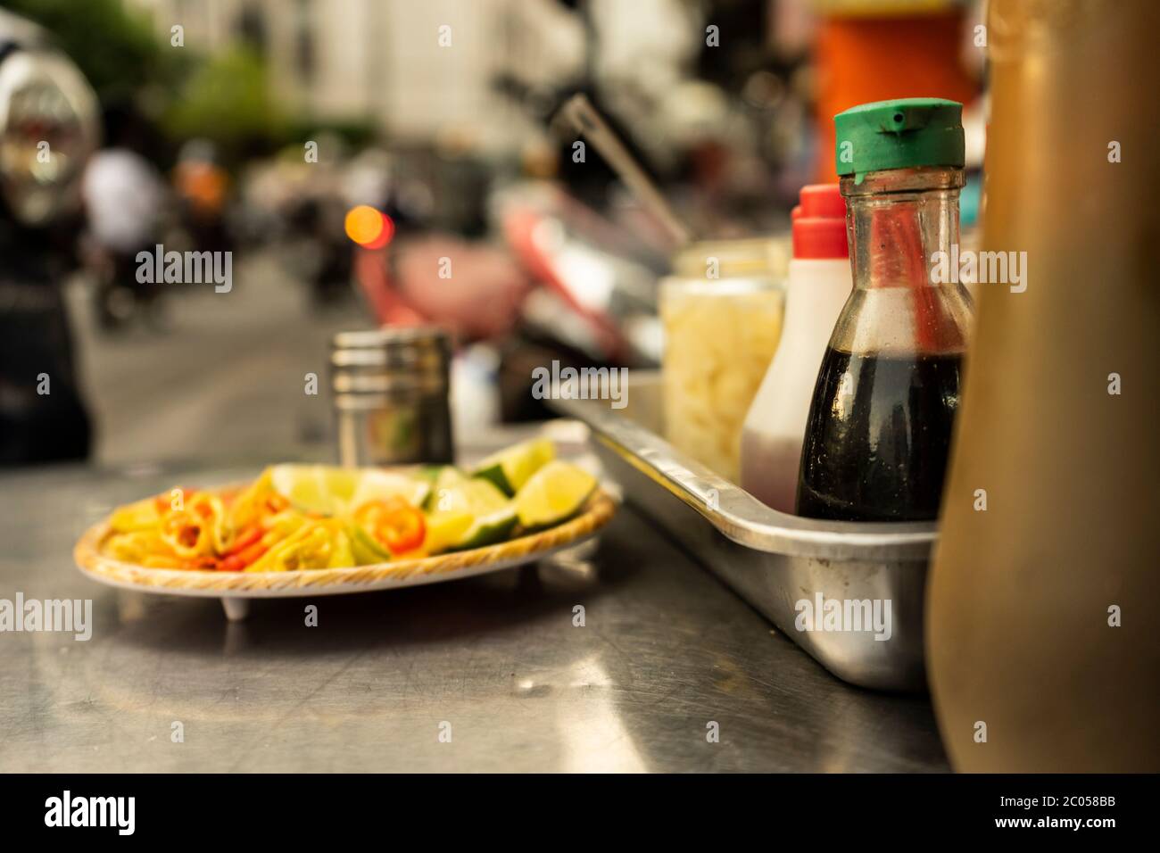 Traditional Vietnamese noodle condiment tray with dish of lemon slices, jar of chili, fish sauce, soy sauce, spoons and chopsticks at street food cart Stock Photo