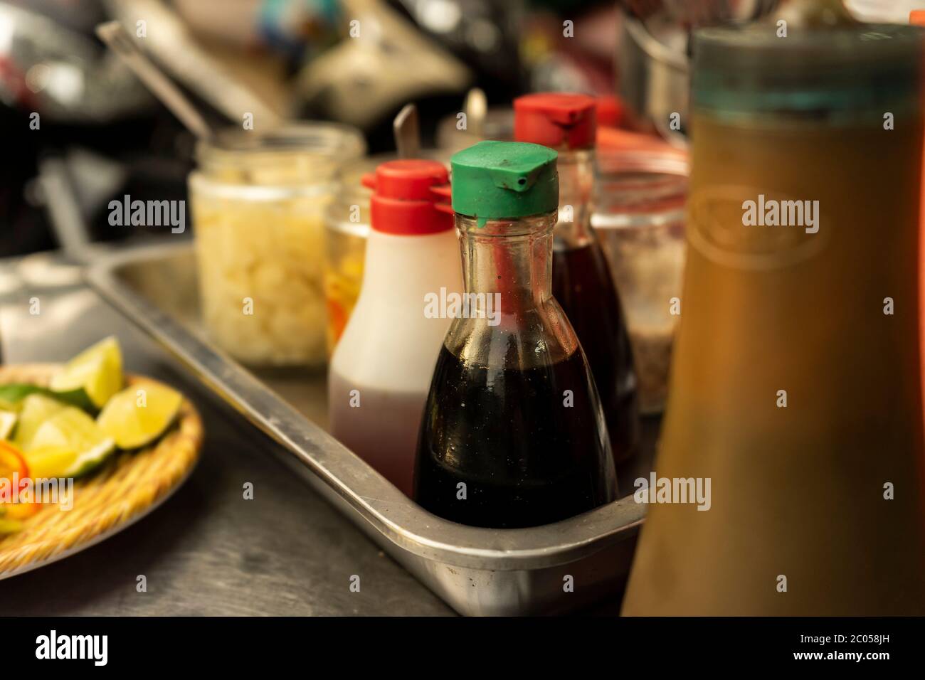 Traditional Vietnamese noodle condiment tray with dish of lemon slices, jar of chili, fish sauce, soy sauce, spoons and chopsticks at street food cart Stock Photo