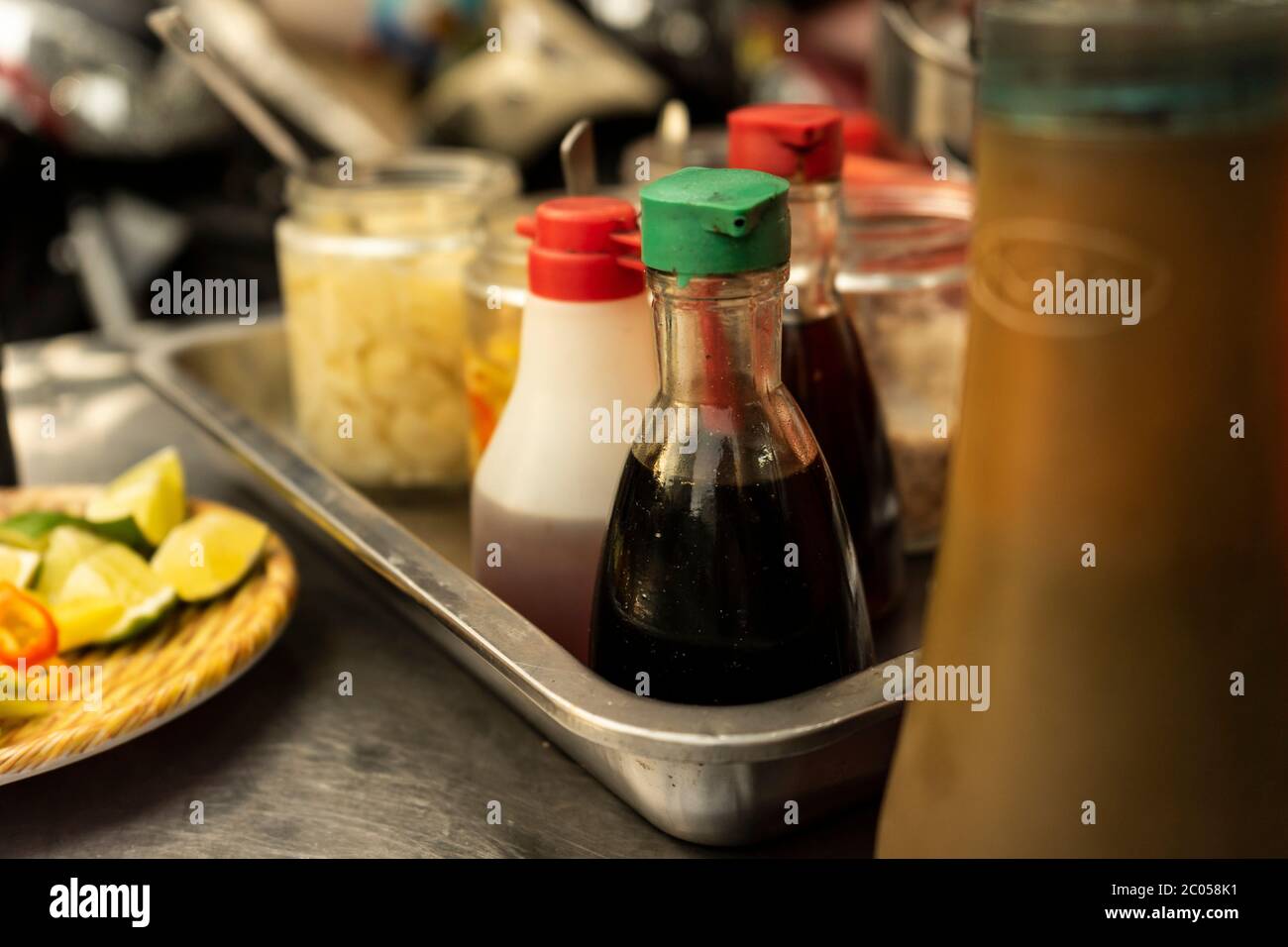 Traditional Vietnamese noodle condiment tray with dish of lemon slices, jar of chili, fish sauce, soy sauce, spoons and chopsticks at street food cart Stock Photo