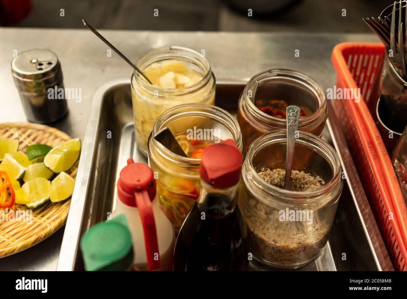 Traditional Vietnamese noodle condiment tray with dish of lemon slices, jar of chili, fish sauce, soy sauce, spoons and chopsticks at street food cart Stock Photo