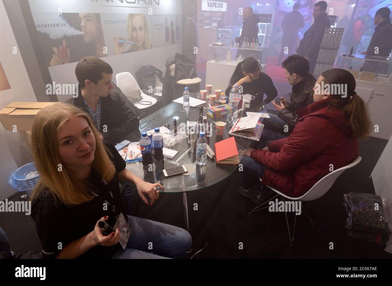Group of young urban hipster girls and boys sit at a table with vape tanks, bottles and discussing e-cigarettes Stock Photo