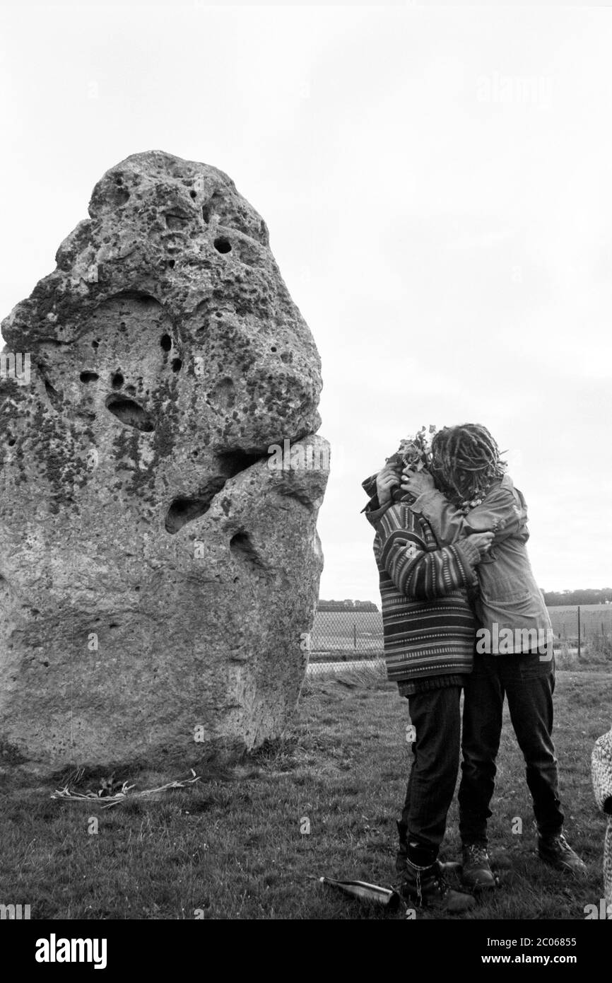 Lovers embrace - Two New Age Travellers kiss next to the Heel Stone at the entrance to Stonehenge. Wiltshire UK. Circa 1990. Stock Photo