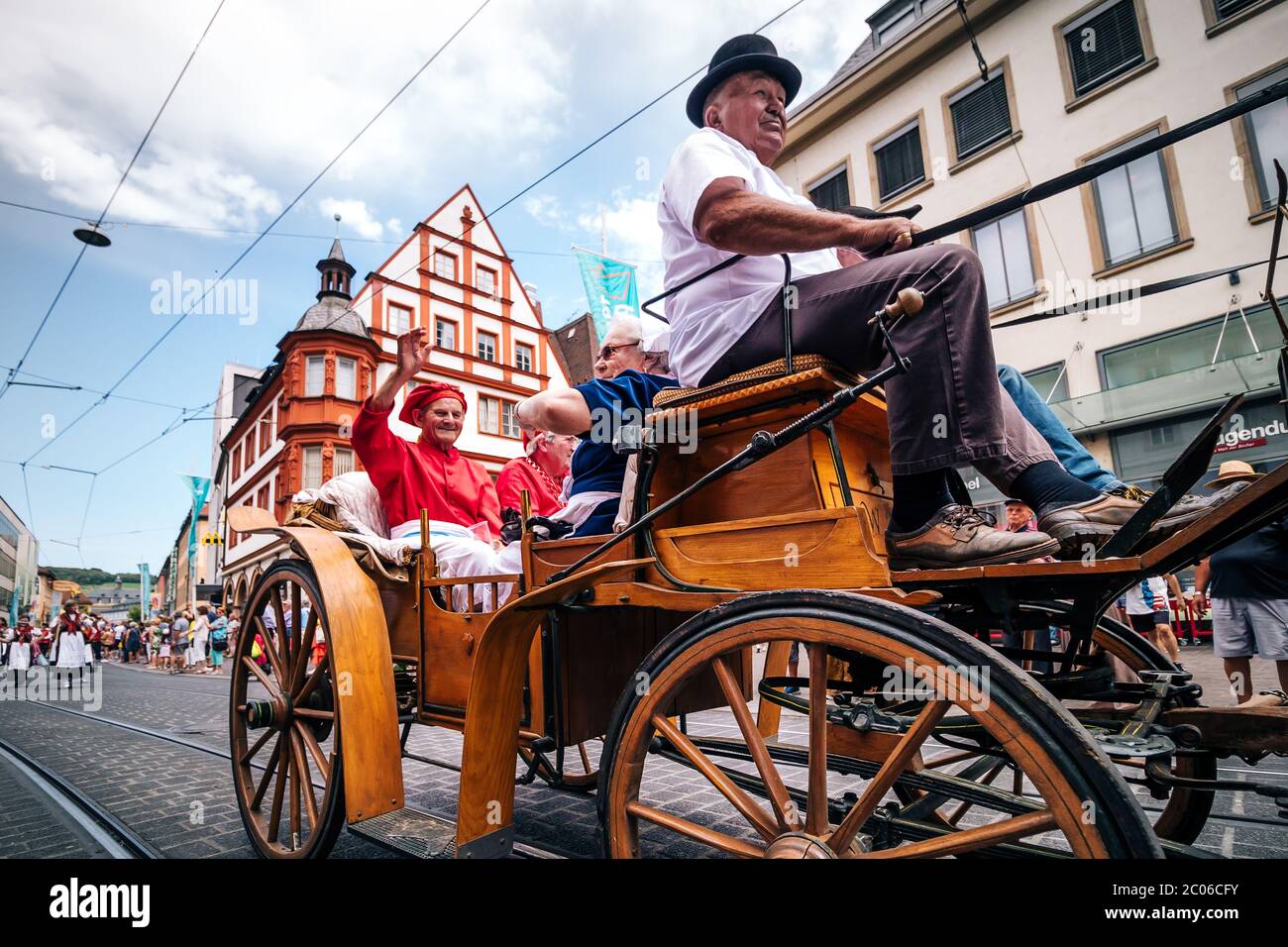 Traditional horse-drawn carriage with happy people at the summer festival opening parade. Kiliani is a 2-weeks-long folk festival with brass music. Stock Photo