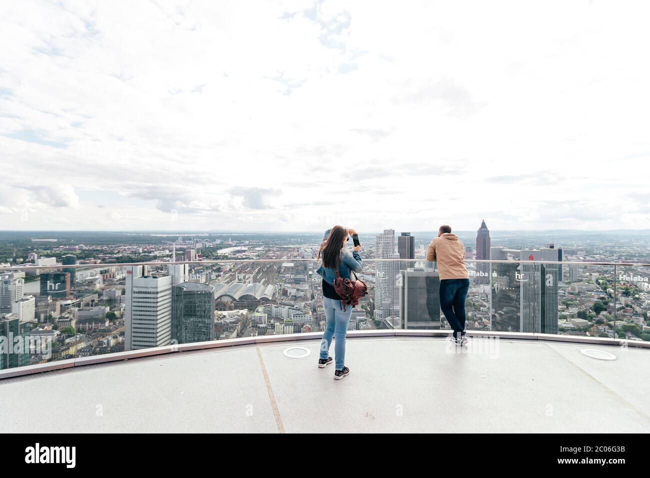 Tourist couple taking photos and enjoying the beautiful skyline view on a sunny Saturday afternoon from the top of Main Tower in Frankfurt am Main. Stock Photo