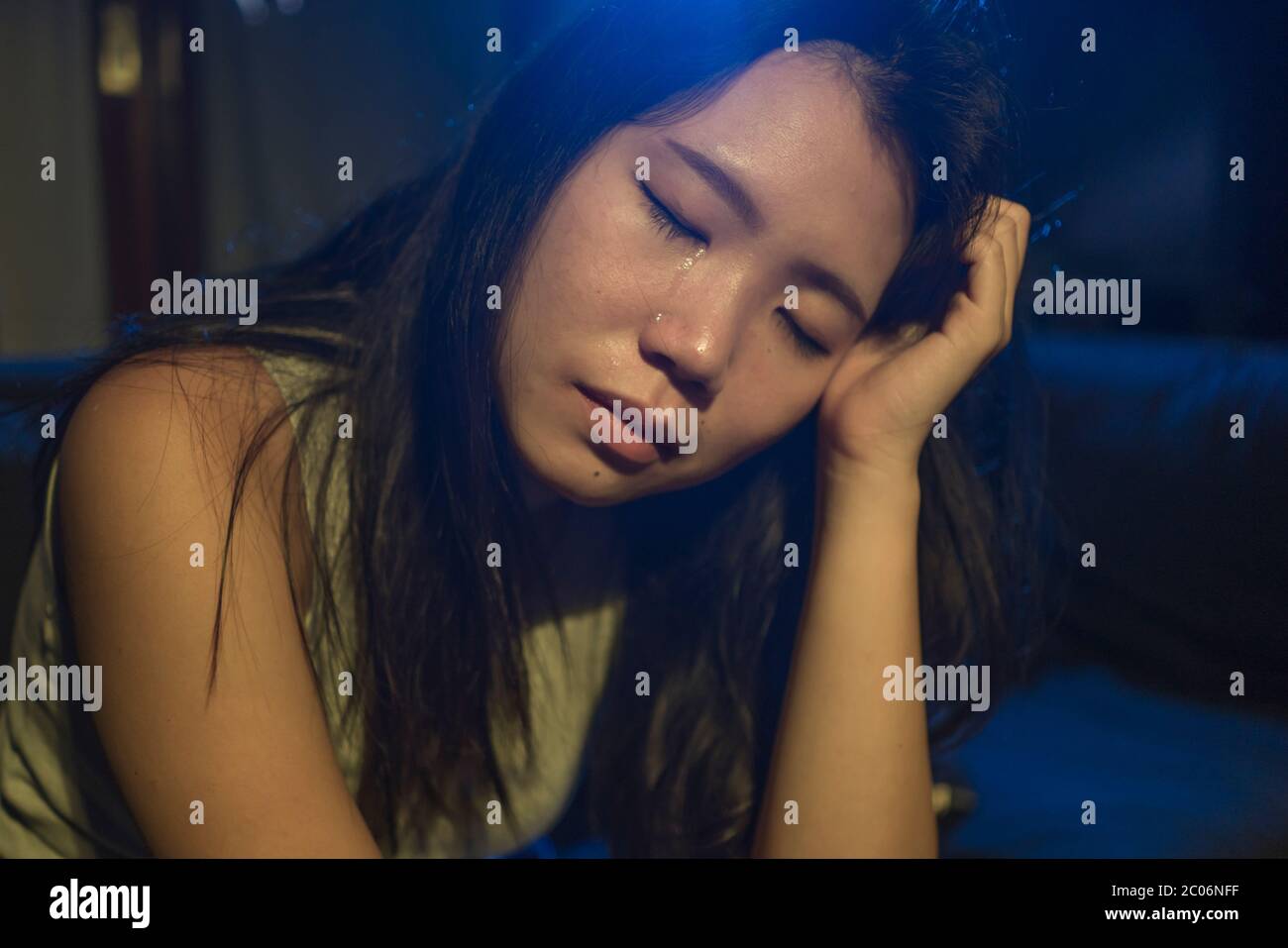 young beautiful sad and depressed Asian Korean woman crying in tears on darkness in pain feeling worried and helpless sobbing desperate at living room Stock Photo