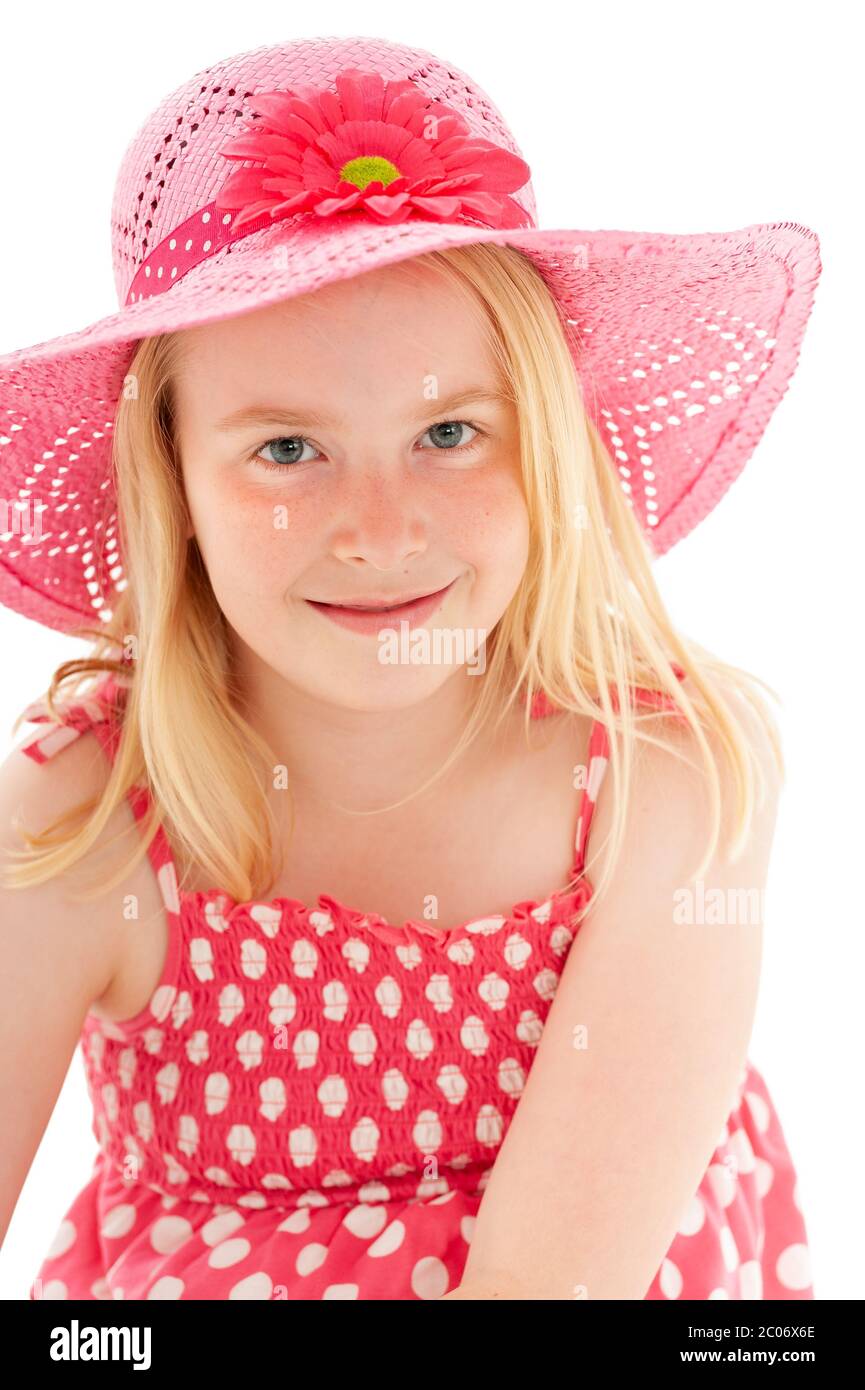 Close up of beautiful young blonde girl with enigmatic smile wearing a big pink floppy hat and looking directly at the camera. Isolated on white studi Stock Photo