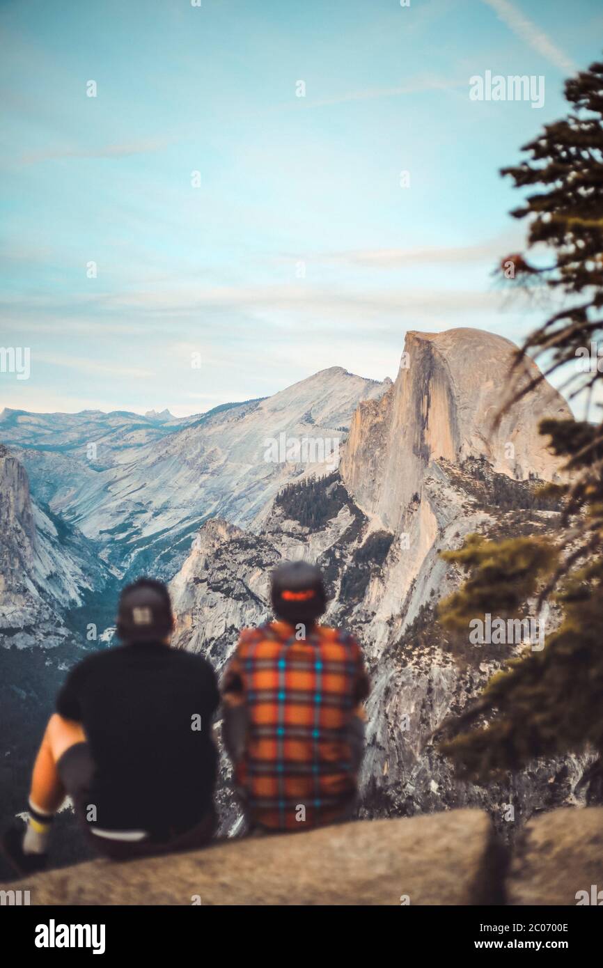 Two people sitting on rock ledge enjoying the view of Half Dome Stock Photo