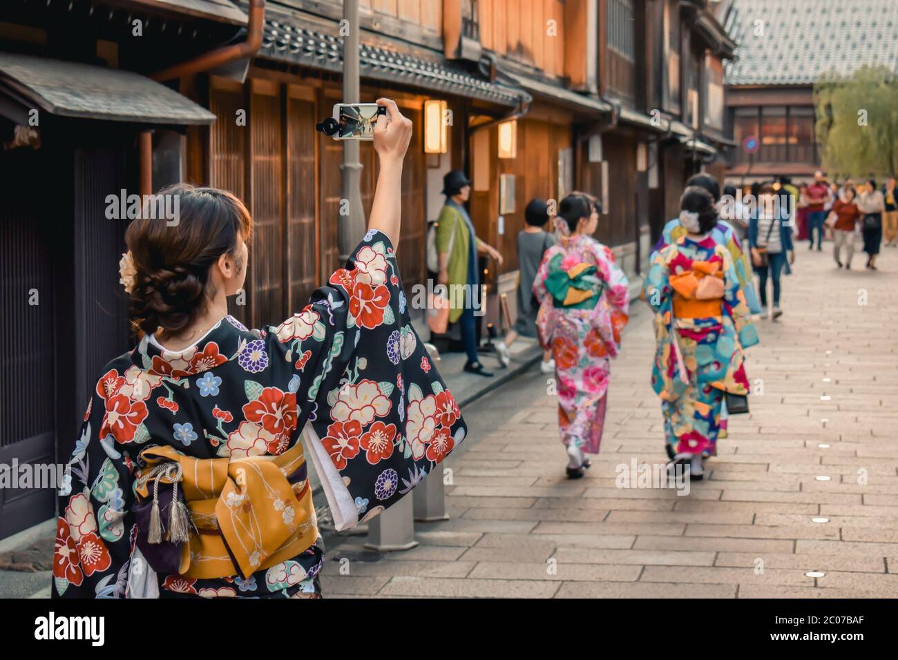 Japanese girl in kimono taking a photo of a traditional street with wooden houses on her cell phone in Kanazawa Japan Stock Photo