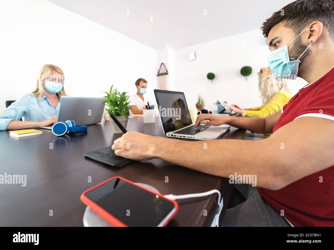 Young people working in modern co-working space wearing surgical mask for preventing corona virus spread Stock Photo